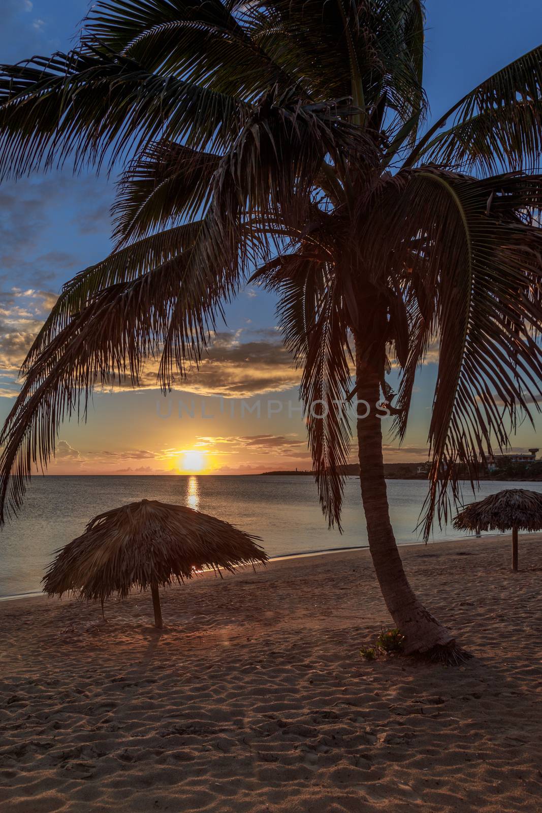 Rancho Luna caribbean beach with palms and straw umbrellas on the shore, sunset view, Cienfuegos, Cuba
