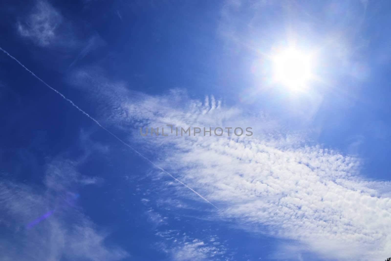 Beautiful view at bright sunbeams with some lens flares and clouds in a blue sky