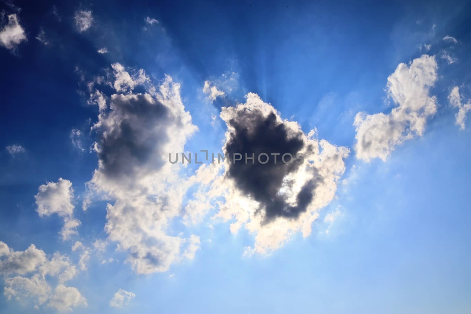 Beautiful view at bright sunbeams with some lens flares and clouds in a blue sky