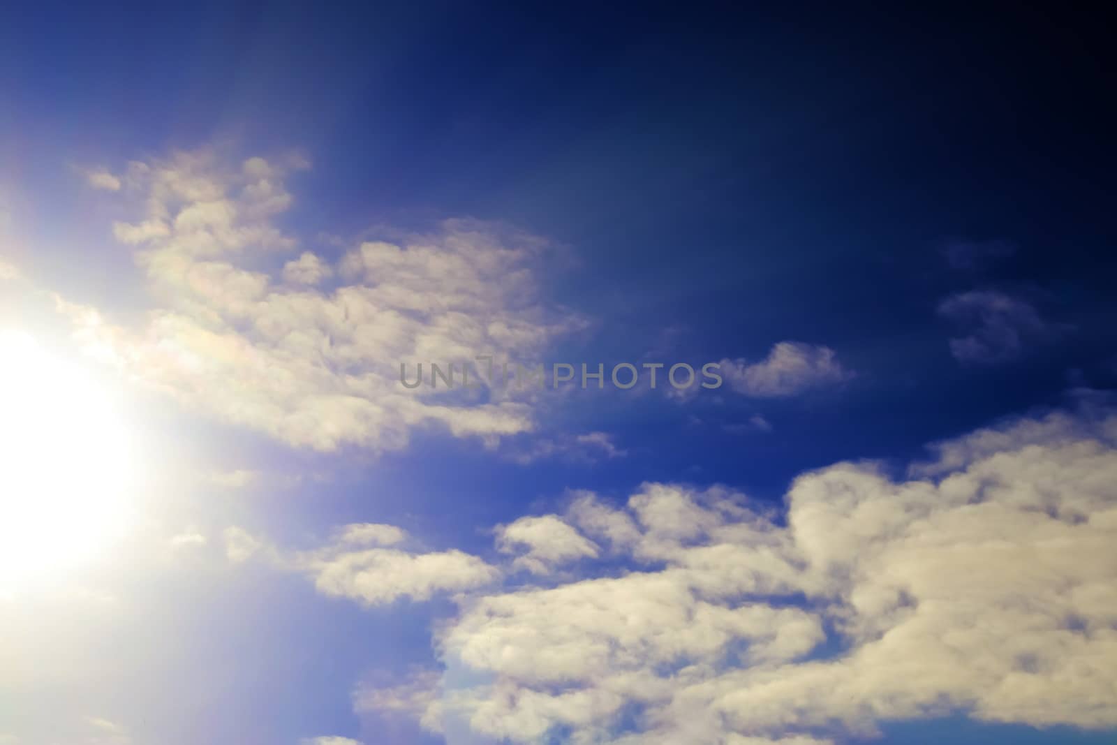 Beautiful view at bright sunbeams with some lens flares and clouds in a blue sky