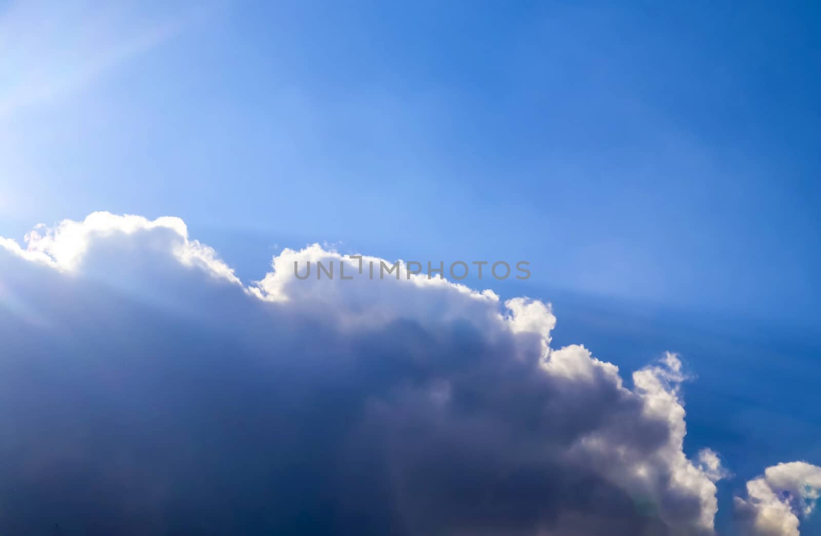 Beautiful view at bright sunbeams with some lens flares and clouds in a blue sky