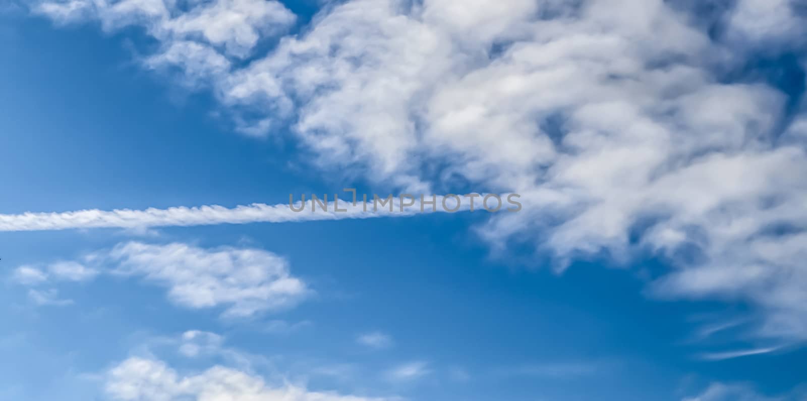 Aircraft condensation contrails in the blue sky inbetween some beautiful clouds
