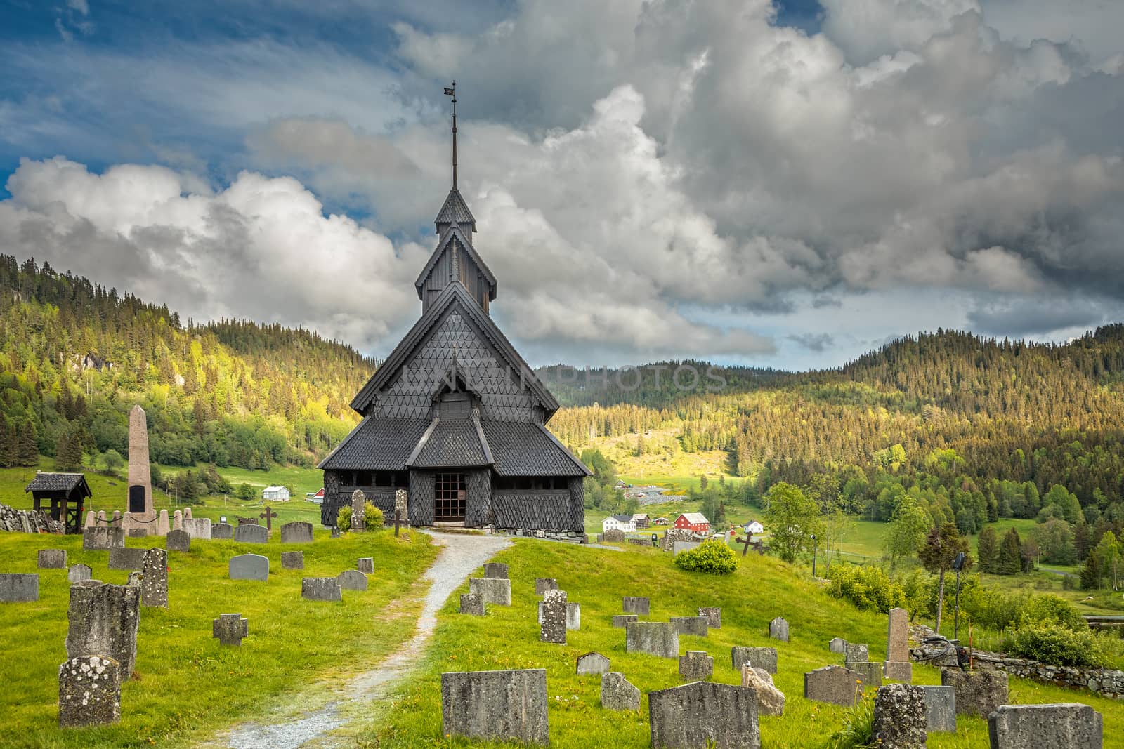 Eidsborg medieval wooden Stave Church and graveyard in front with green forest and cloud sky in the backround, Tokke, Telemark county, Norway