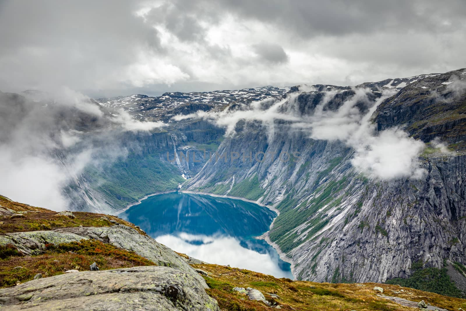 Blue lake surrounded by steep cliffs hiding in clouds, Odda, Hordaland county, Norway