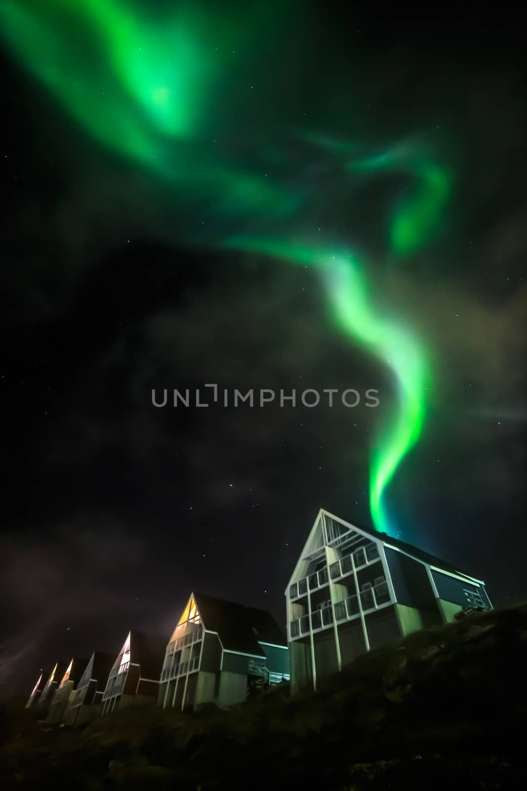 Green bright northern lights partially hidden by the clouds over Inuit living houses, Nuuk city, Greenland