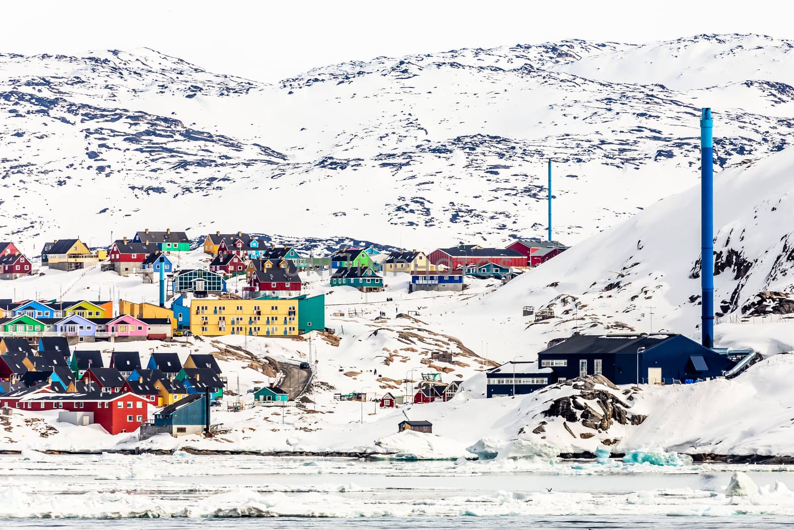 Arctic city panorama with colorful Inuit cottages and powerplant on the rocky hills covered in snow and mountain in the background, Ilulissat, Avannaata municipality, Greenland