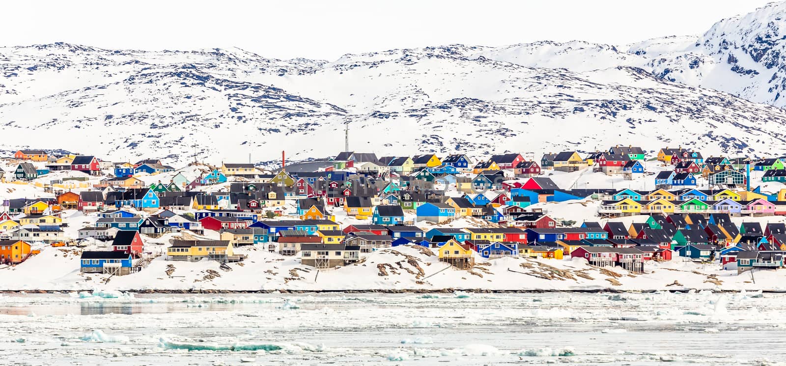 Arctic city center panorama with colorful Inuit houses on the rocky hills covered in snow with snow and mountain in the background, Ilulissat, Avannaata municipality, Greenland