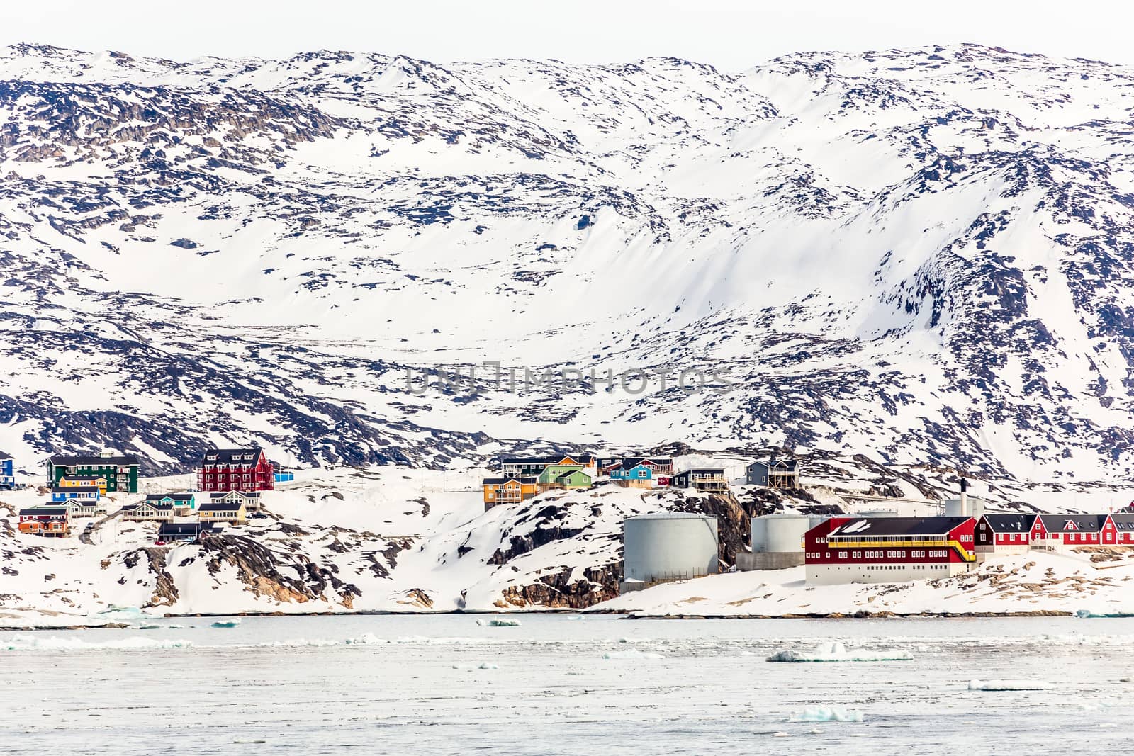 Arctic city panorama with colorful Inuit cottages and oil factory on the rocky hills covered in snow and mountain in the background, Ilulissat, Avannaata municipality, Greenland