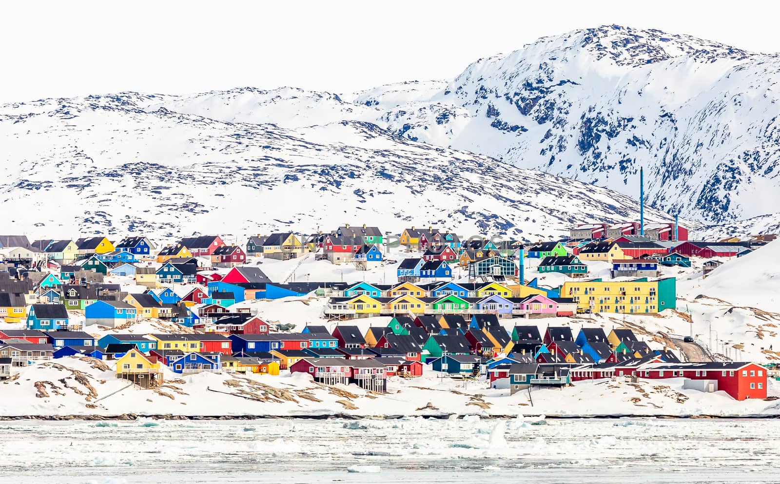 Arctic city panorama with colorful Inuit houses on the rocky hills covered in snow with snow and mountain in the background, Ilulissat, Greenland