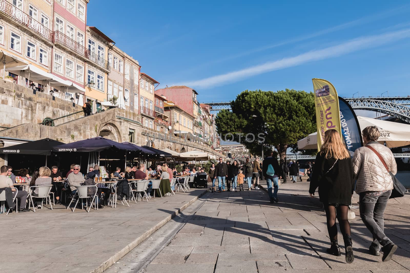 Porto, Portugal - November 30, 2018: Street atmosphere near the Dom Luiz bridge with its café terrace and its traders where people are walking on an autumn day