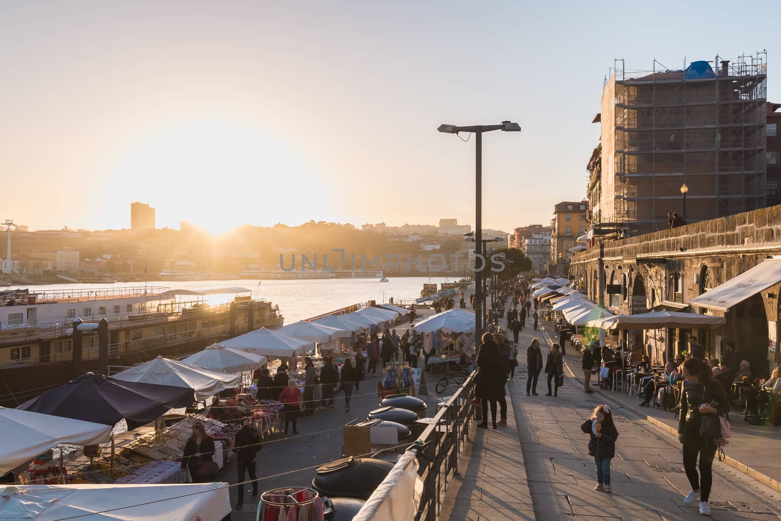 Porto, Portugal - November 30, 2018: Street atmosphere near the Dom Luiz bridge with its café terrace and its traders where people are walking on an autumn day