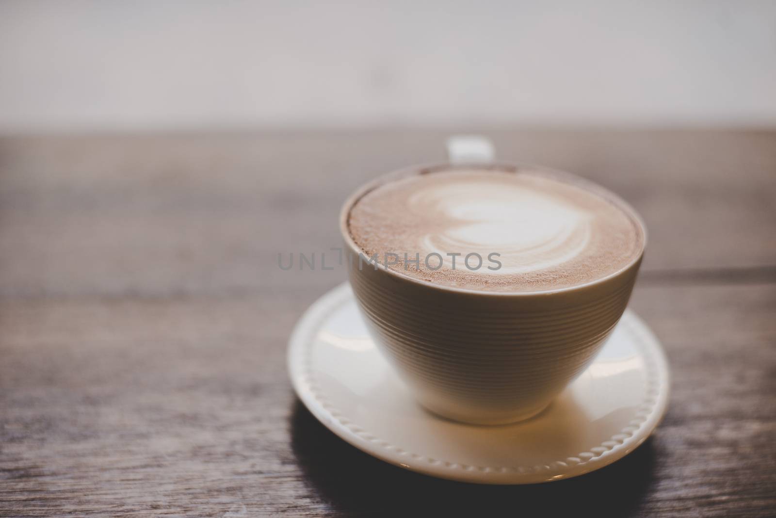 Vintage latte art coffee with heart shape on wooden table.