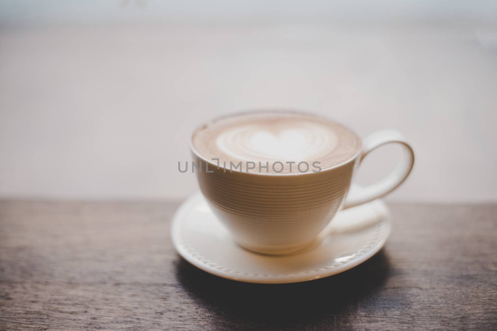 Vintage latte art coffee with heart shape on wooden table.