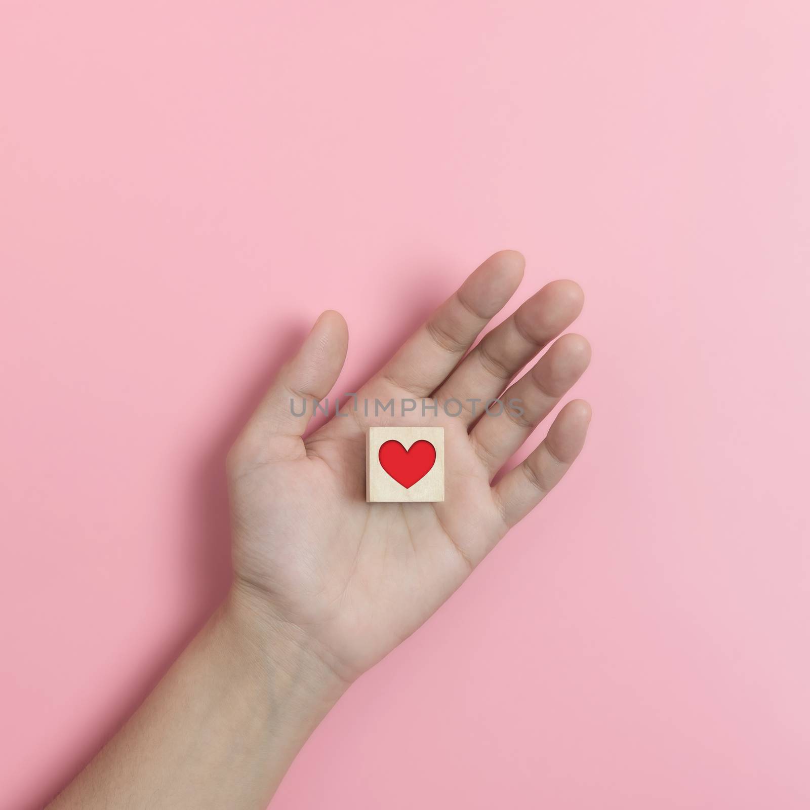Hands holding Wood cube with  red heart on pink background. Valentines day, Love concepts.