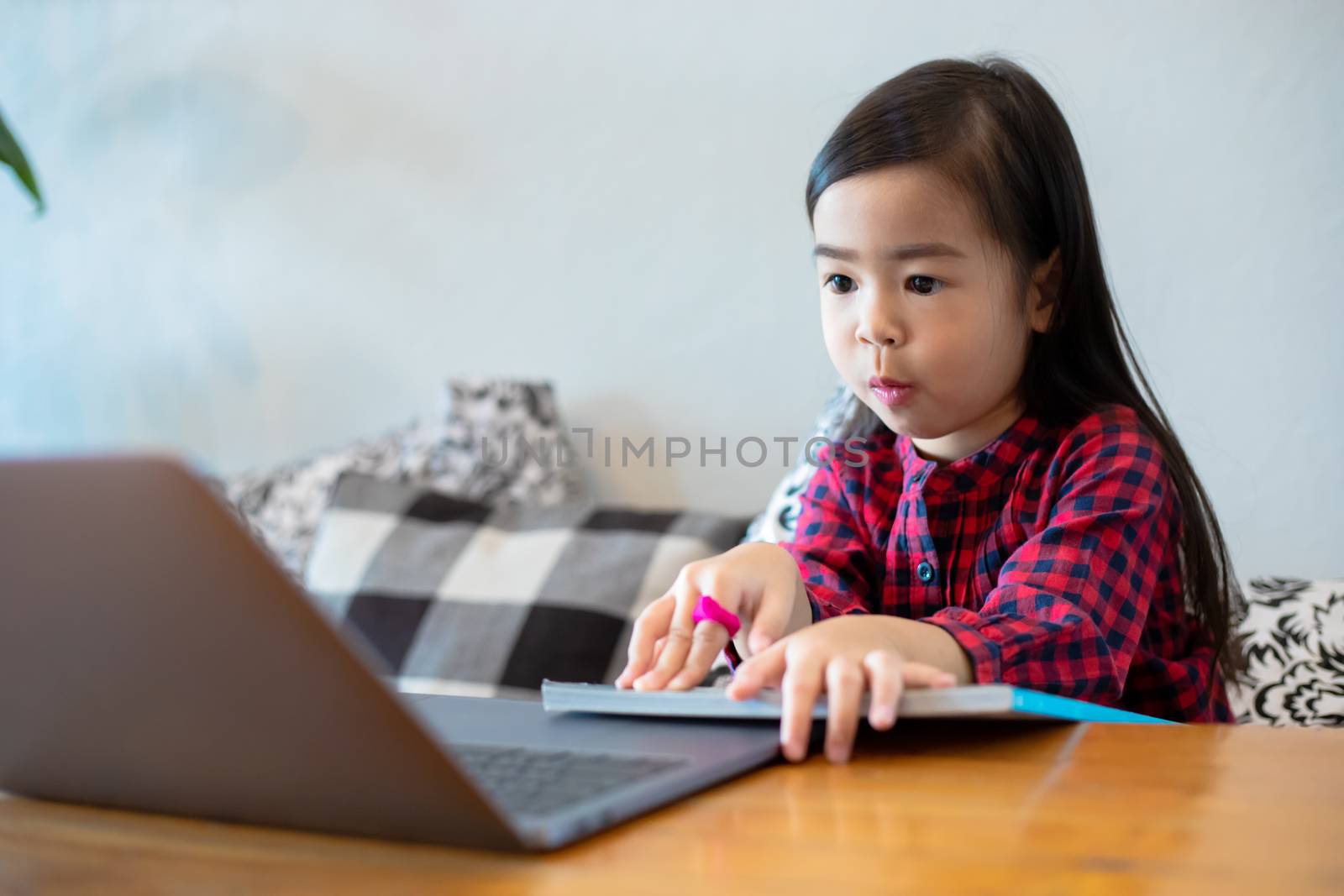 Asian girl or daughters use notebooks and technology for online learning during school holidays and watching cartoons at home. Educational concepts and activities of the family