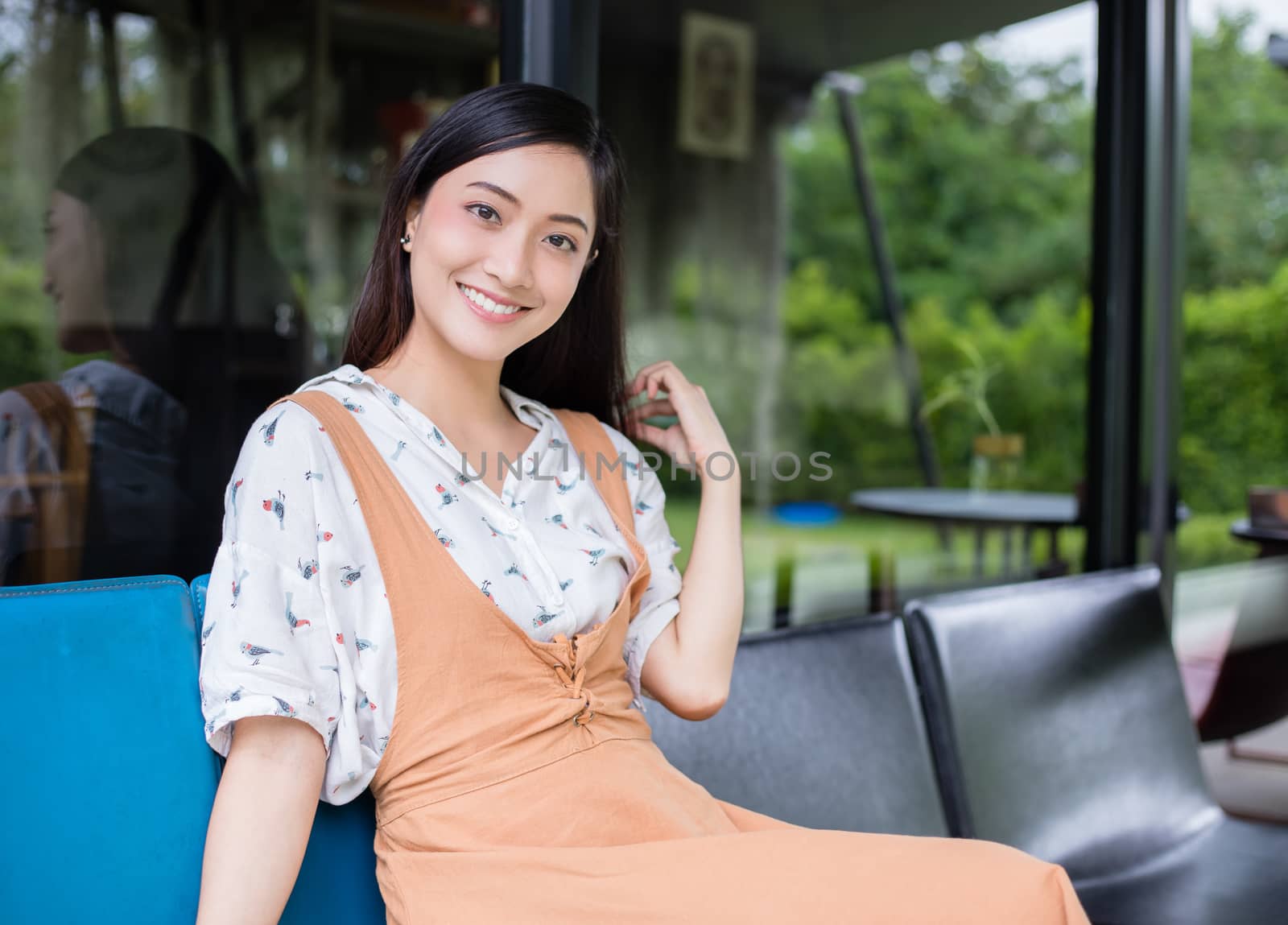 Cute Asian woman sits on the sofa or chair and looks at the camera and smiles happy in portraits at home during relax time.