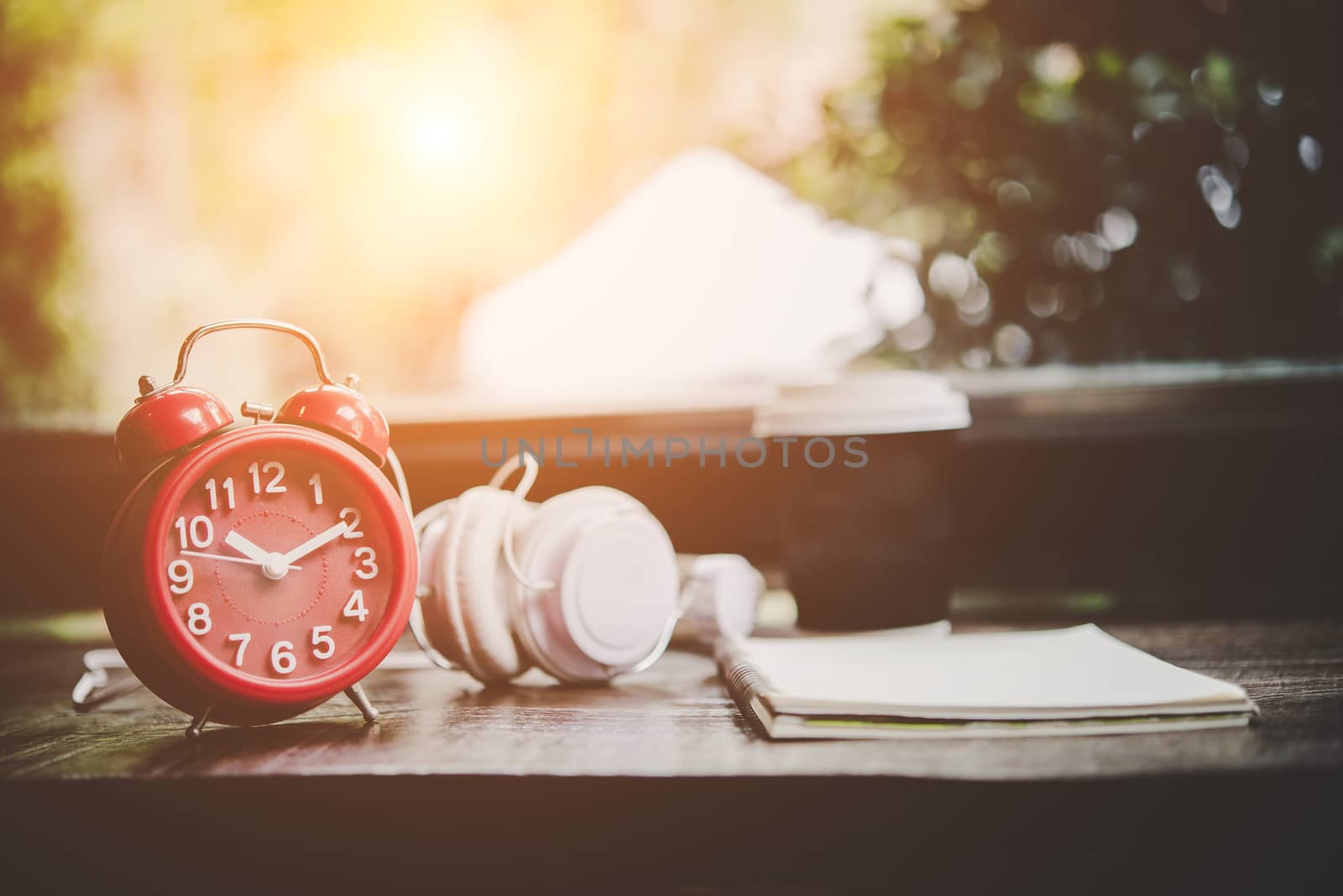 Paper cup of coffee,notebook and Red alarm clock with headphone on the wood table, Relaxing time. Lifestyle concept. 