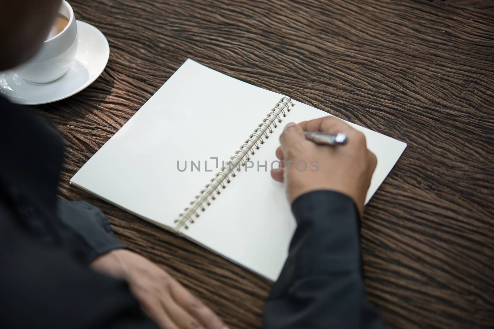 Young man writing on a notebook working on a rustic wooden table.