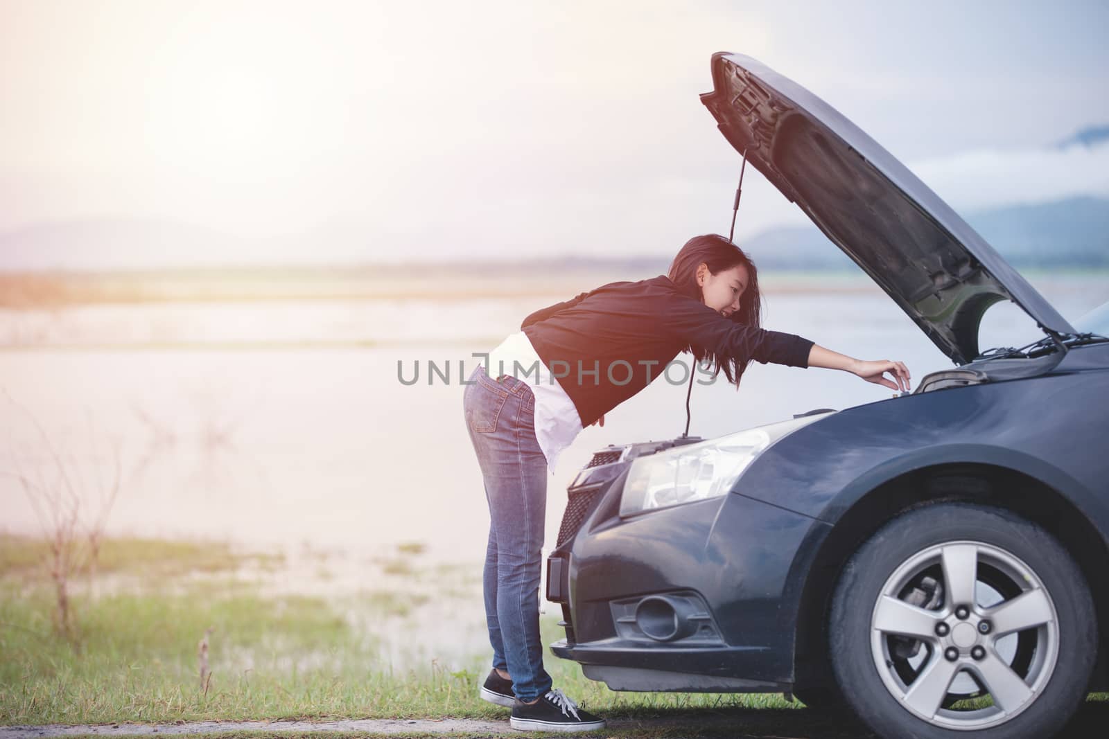 Asian woman checking broken down car on street