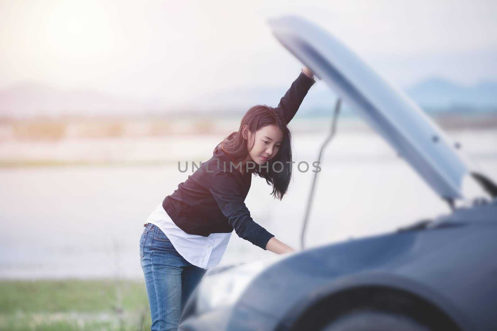 Asian woman checking broken down car on street