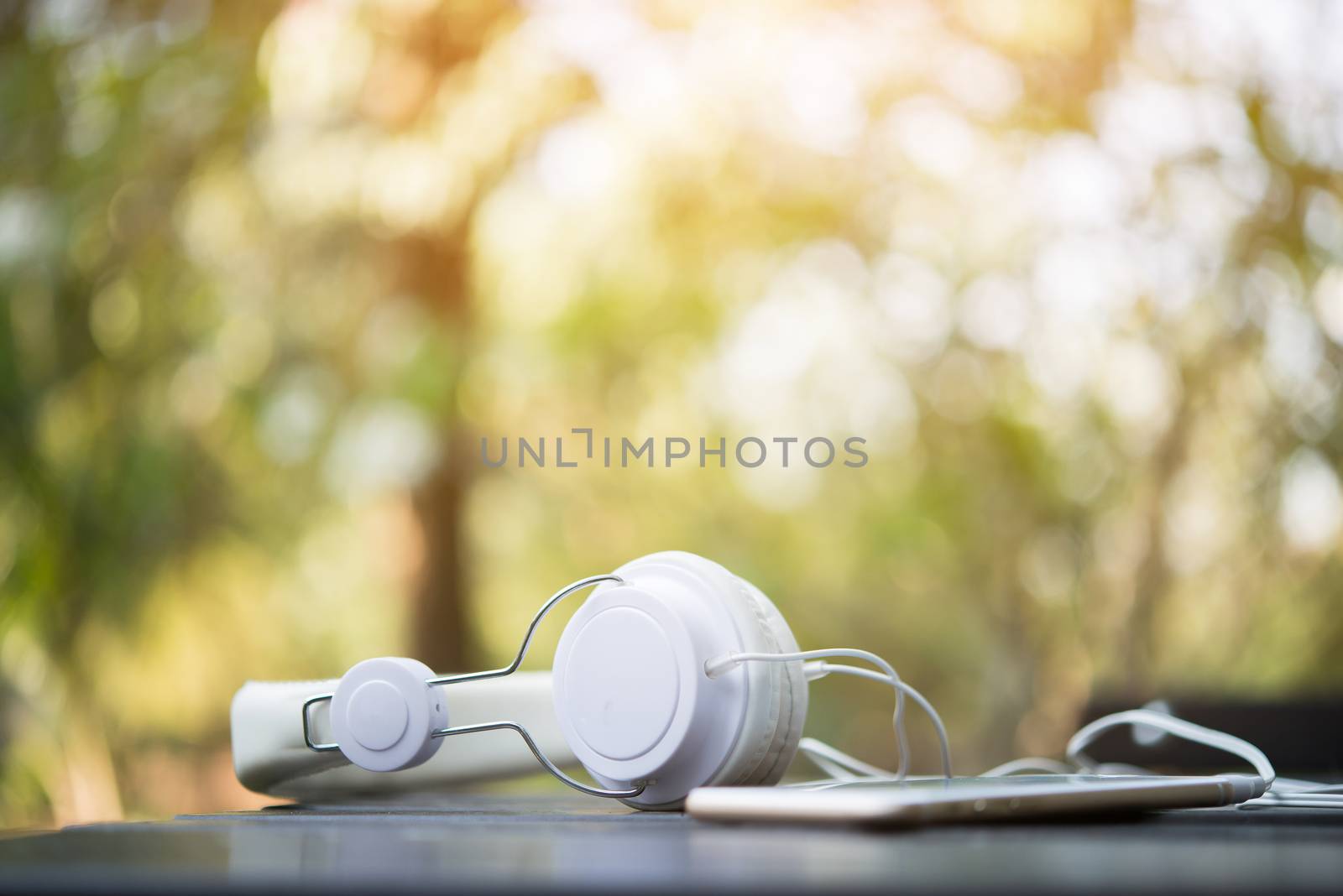 Mobile phone with headphone on wooden table with nature background - Vintage Filter.