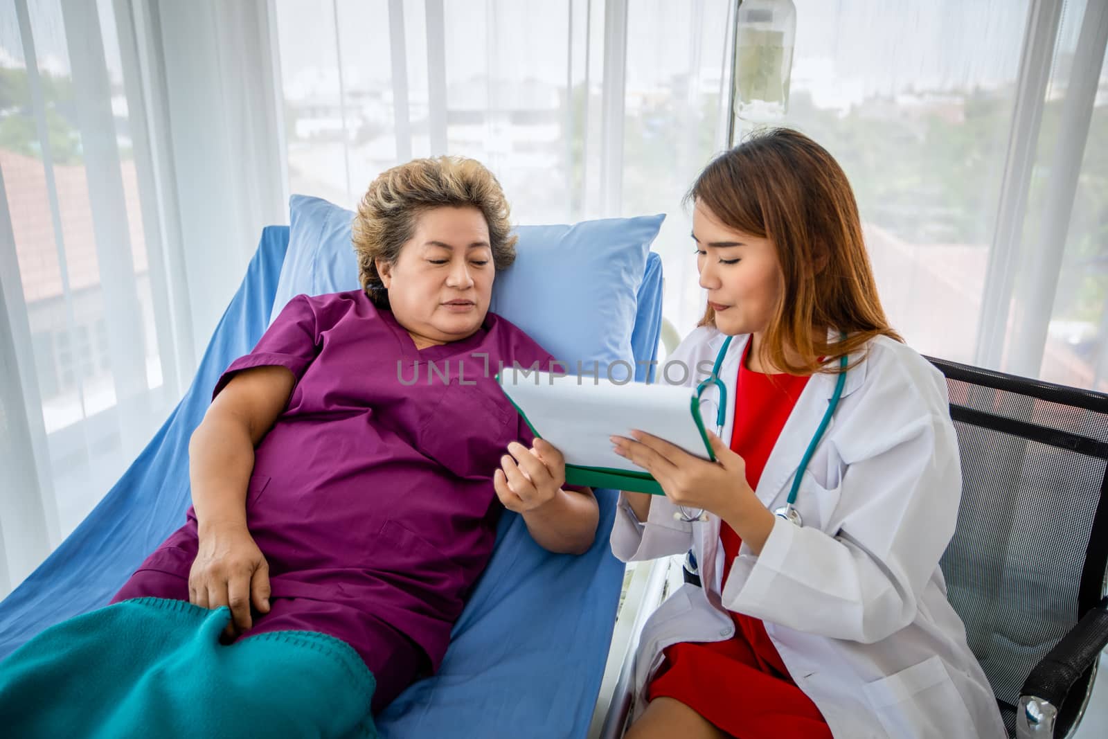 Doctor meeting and explaining medication to old woman patient lying in bed at Hospitals