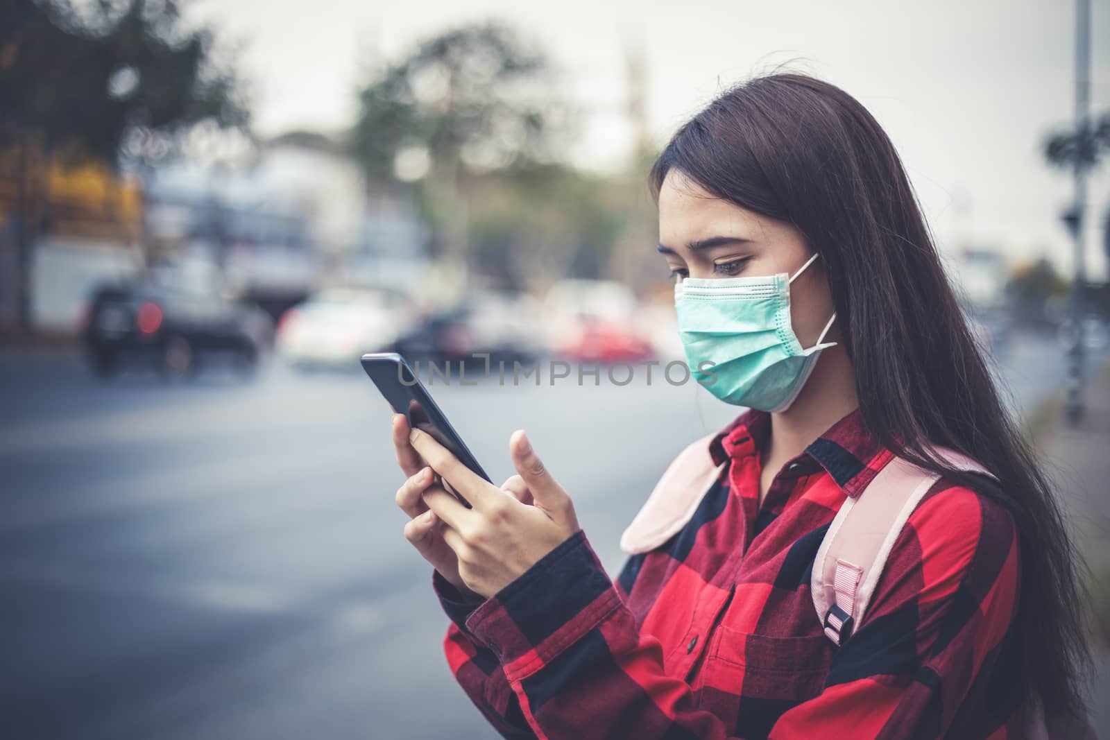 Asian Young woman using smart phone in the city wearing face mask because of air pollution, particulates and for protection flu virus, influenza, coronavirus