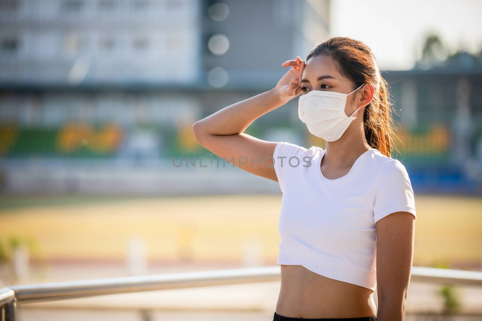 Asian Young fitness sport woman is resting tired and she wears a mask for protective Dust and pollution on city
