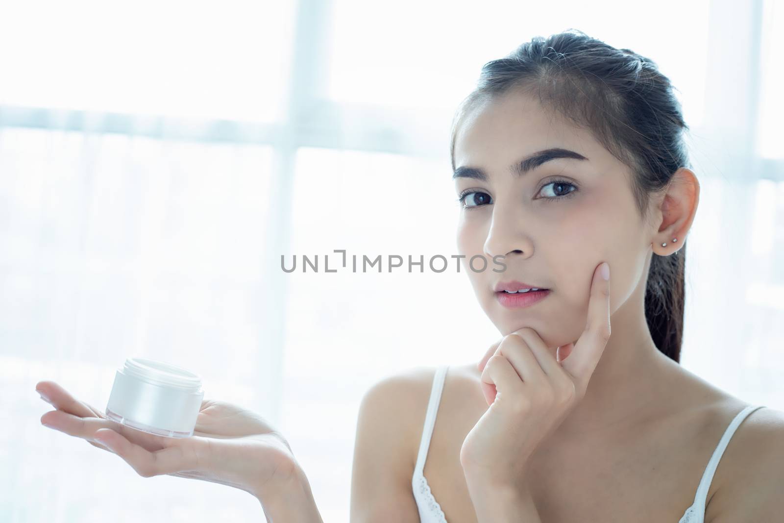 A beautiful woman asian using a skin care product, moisturizer or lotion taking care of her dry complexion. Moisturizing cream in female hands .