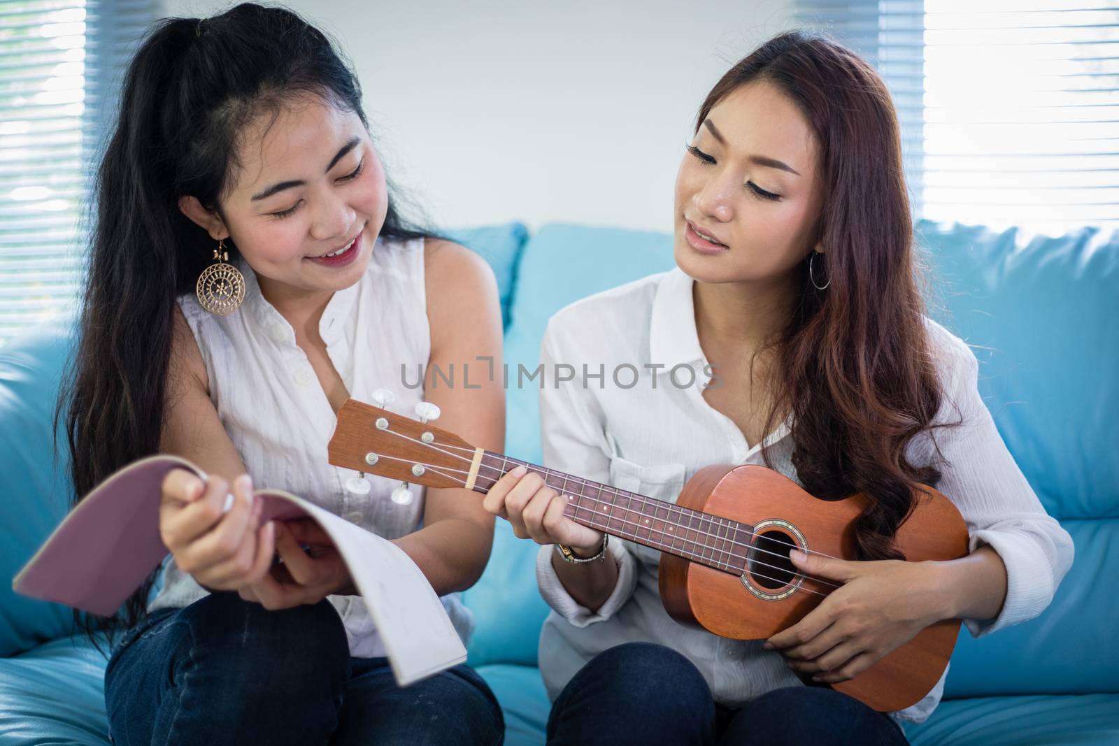 Two asia women are having fun playing ukulele and smiling at home for relax time