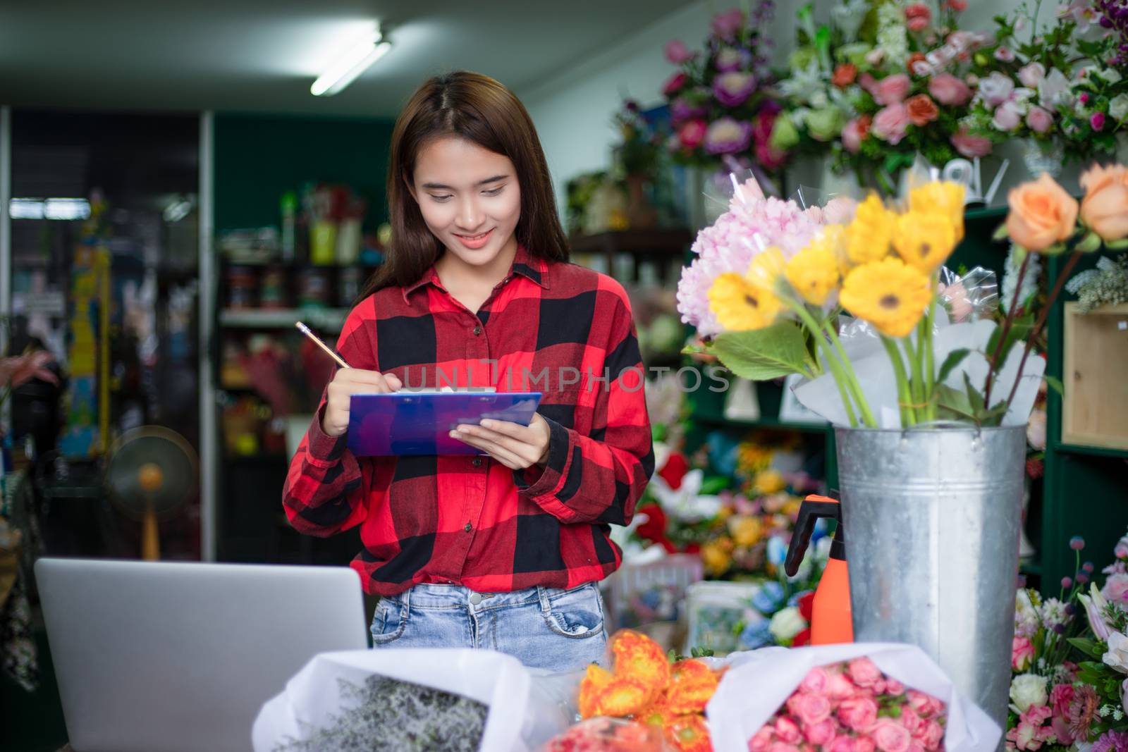 Asian Woman Florist Small Business Flower Shop Owner and She is using her telephone and laptop to take orders for her store.