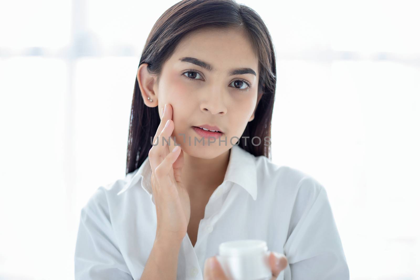 A beautiful woman asian using a skin care product, moisturizer or lotion taking care of her dry complexion. Moisturizing cream in female hands .
