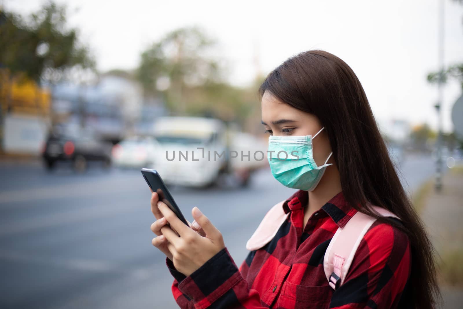 Asian Young woman using smart phone in the city wearing face mask because of air pollution, particulates and for protection flu virus, influenza, coronavirus