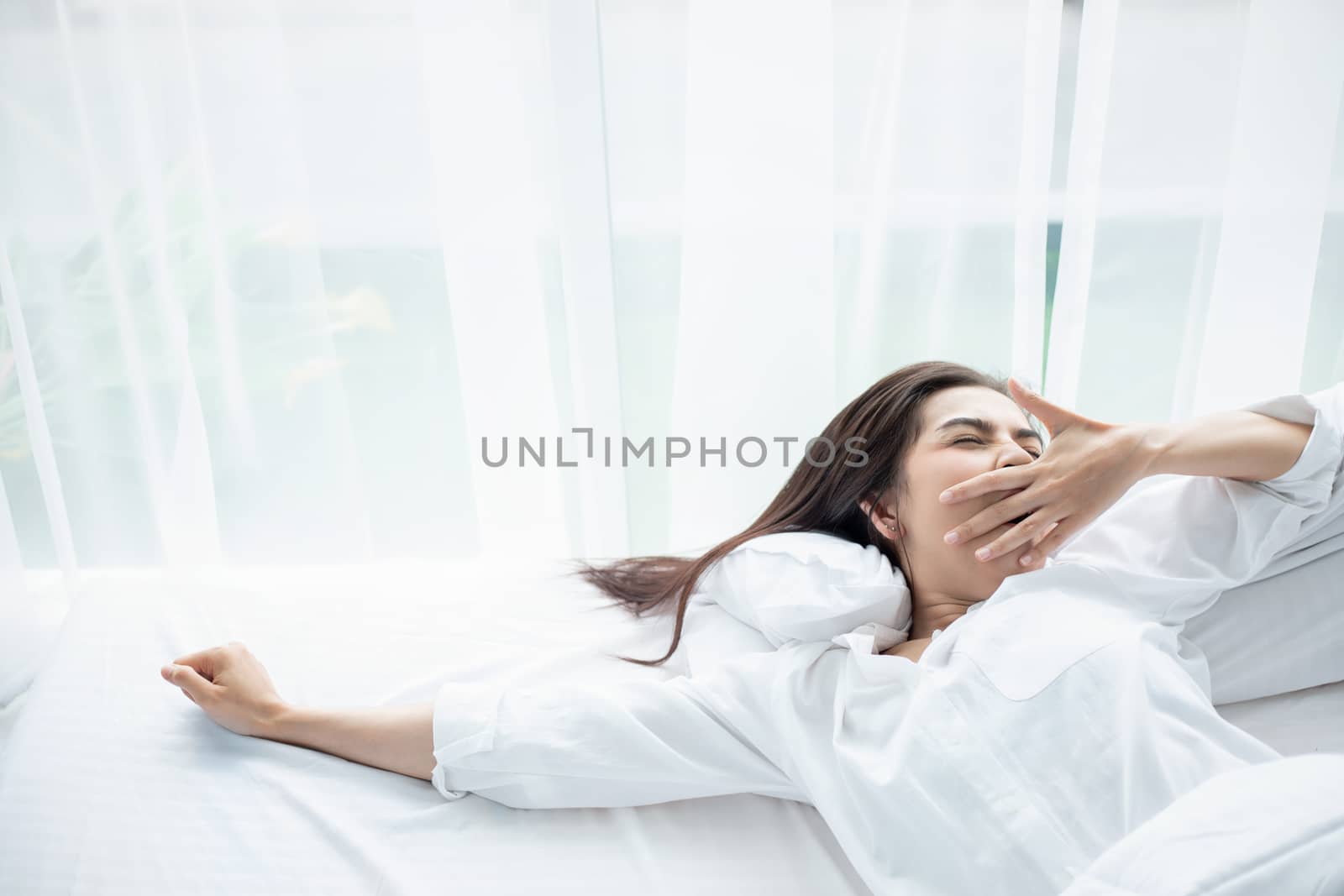 Asian woman Beautiful young smiling woman sitting and sleeping in white bed and stretching in the morning at bedroom after waking up in her bed fully rested