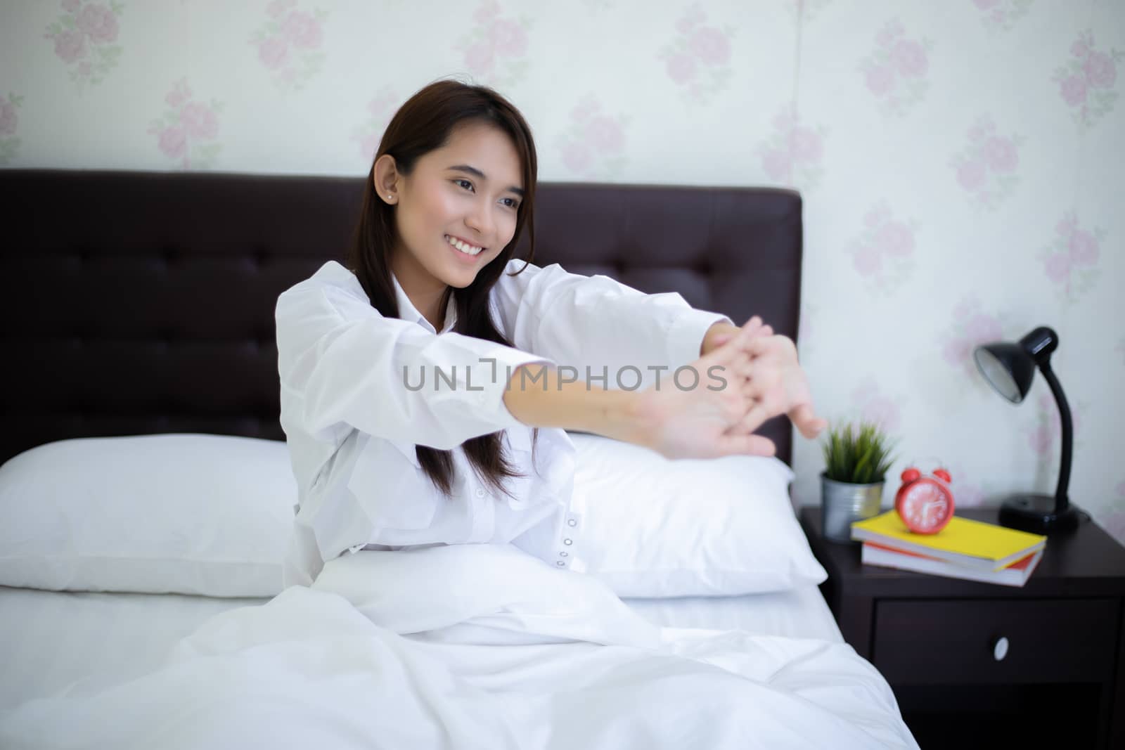 Asian woman Beautiful young smiling woman sitting on bed and stretching in the morning at bedroom after waking up in her bed fully rested