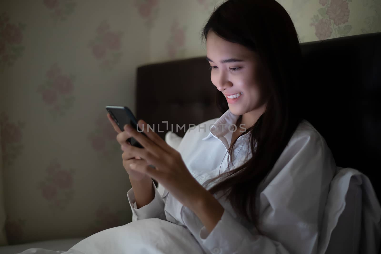 Asian woman using a mobile phone on night at the bed.She smiles and enjoys at home.