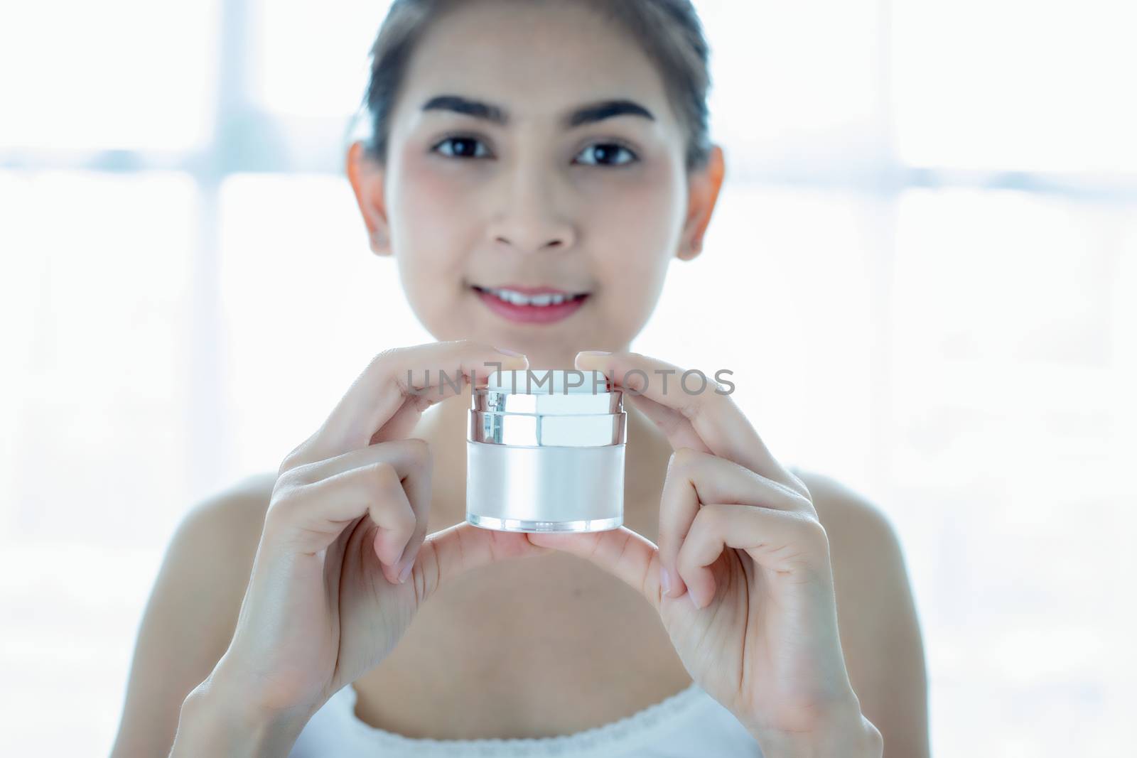 A beautiful woman asian using a skin care product, moisturizer or lotion taking care of her dry complexion. Moisturizing cream in female hands .