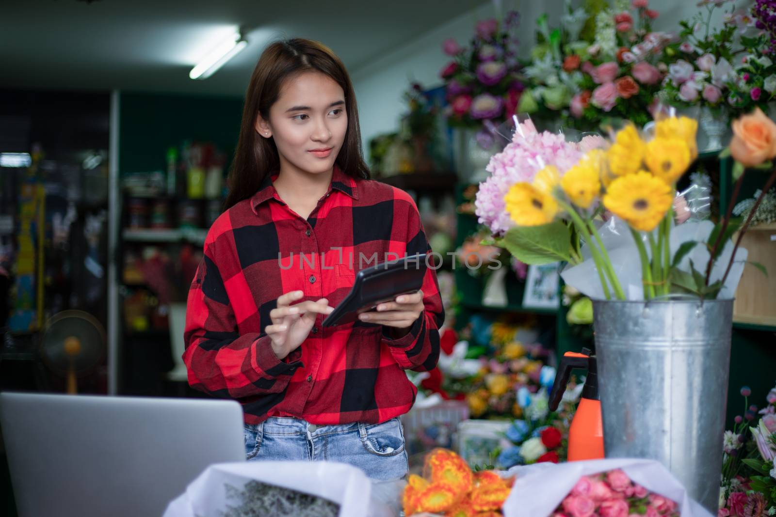 Asian Woman Florist Small Business Flower Shop Owner and She is using her Calculator and laptop to take orders for her store.