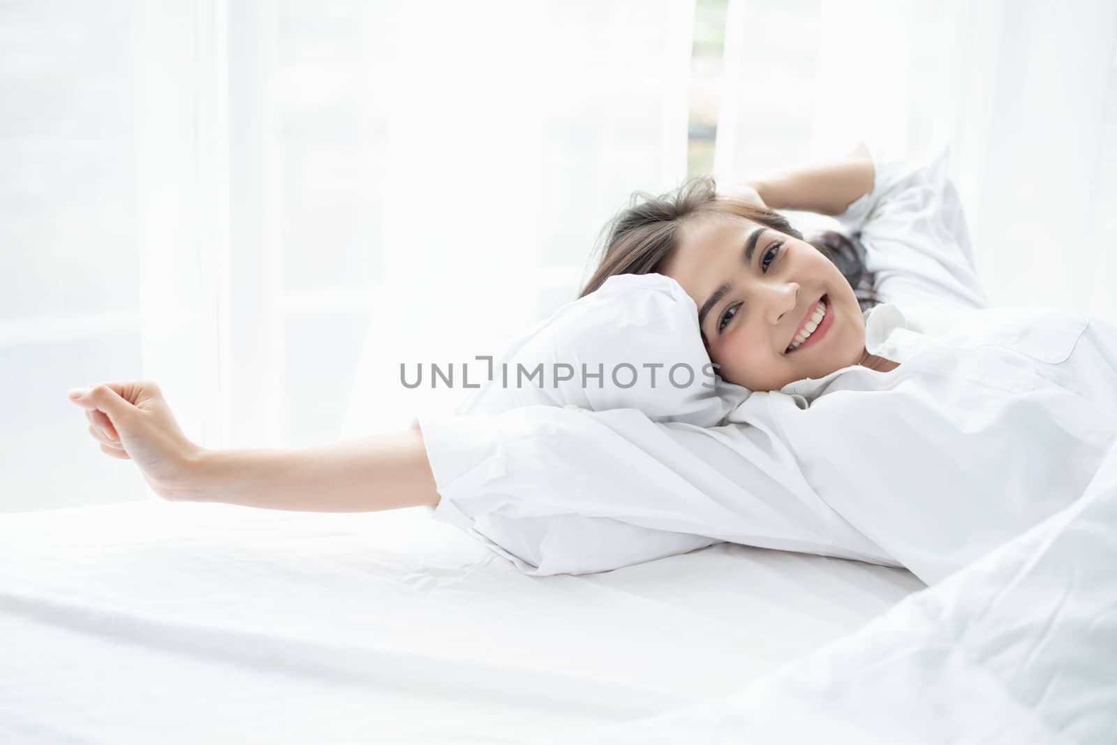 Asian woman Beautiful young smiling woman sitting and sleeping in white bed and stretching in the morning at bedroom after waking up in her bed fully rested