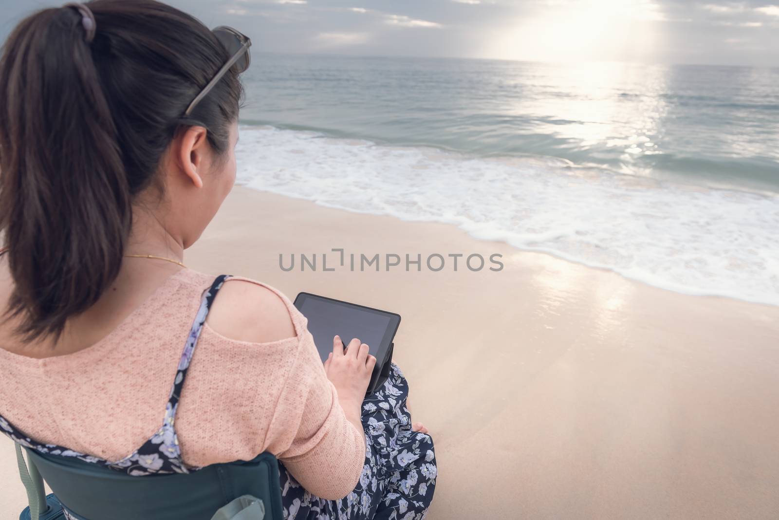 Freelancer Woman is Working on Tablet While Travel Vacation Trip at The Beach, Smart Woman is Using Tablet for Communication and Entertainment at Outdoor Sand Beach. Freelance and Relaxation Concept.