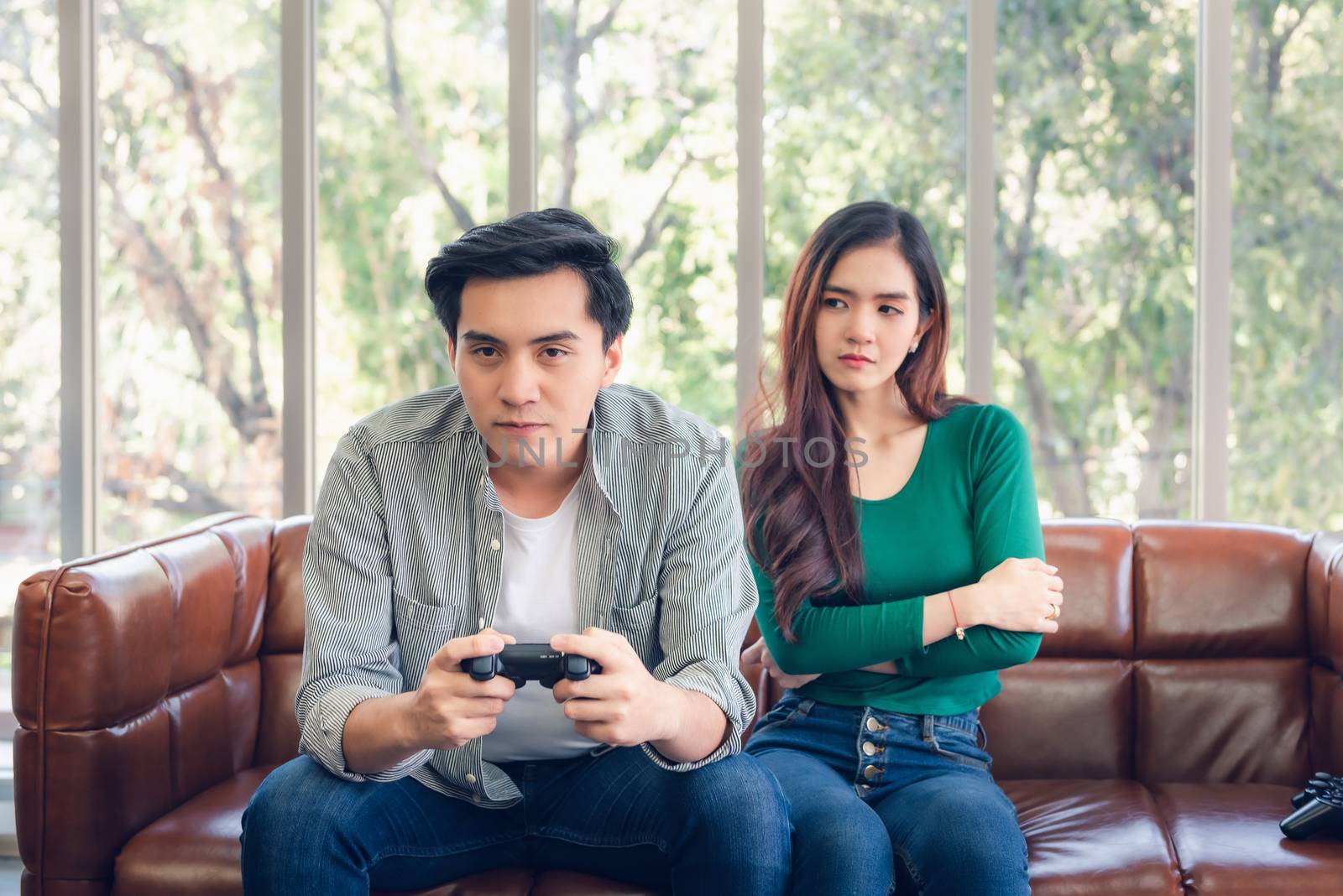 Portrait of Woman Feeling Offended With Her Boyfriend When He Playing Video Games While Sitting on The Couch in Living Room. Couple Love Relationship and Lifestyles Concept. by MahaHeang245789