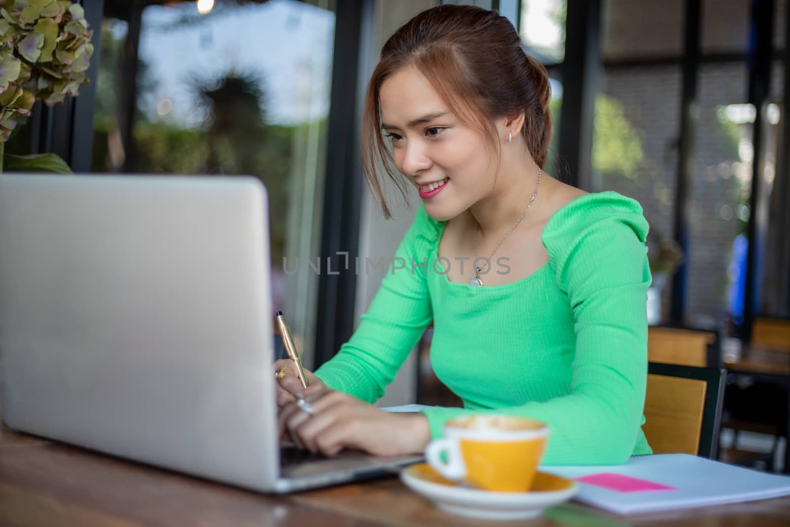 Asian businesswomen smiling and using notebook for analysis documents and graph financial diagram working and she is drinking coffee at coffee shop