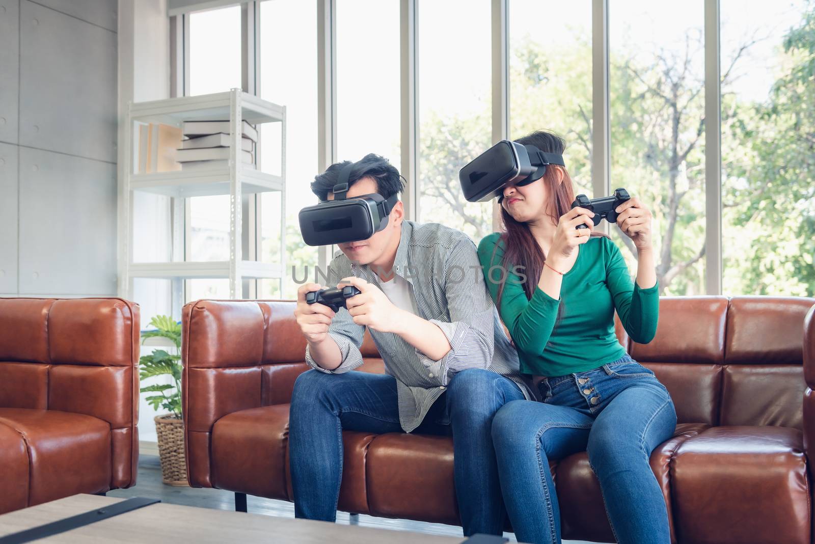 Young Couple Having Fun While Playing Virtual Reality Game Together in Their Home. Couple Love Having Enjoyment With Electronic VR Goggles Gaming on Couch. Entertainment Innovation/Lifestyles Concept by MahaHeang245789