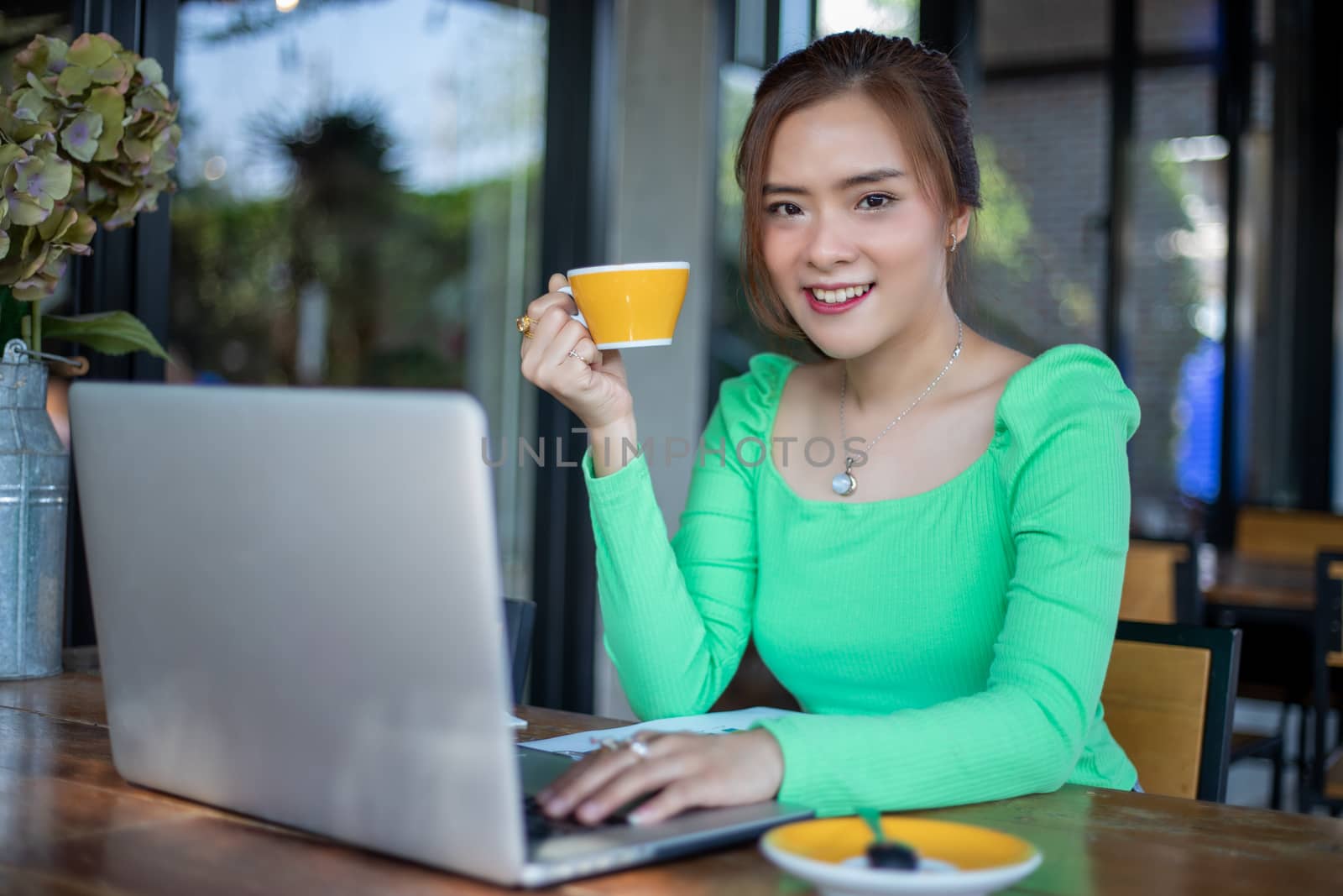 Asian businesswomen smiling and using notebook for analysis documents and graph financial diagram working and she is drinking coffee at coffee shop