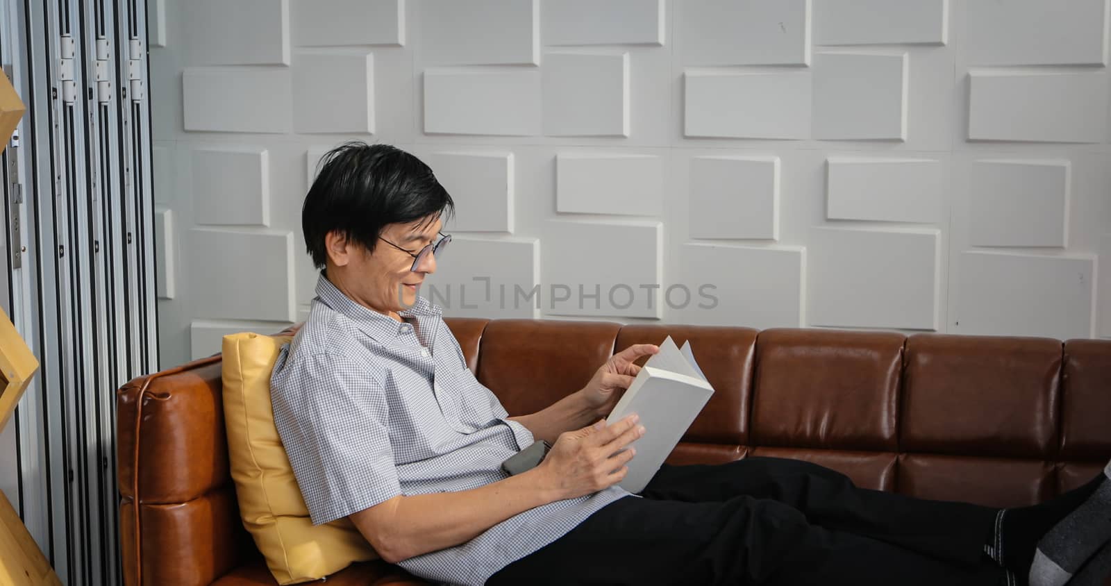 Senior Asian man reading book on sofa in living room at home ,Portrait of Asian elderly man is Relaxing and Happiness With Read a Magazine