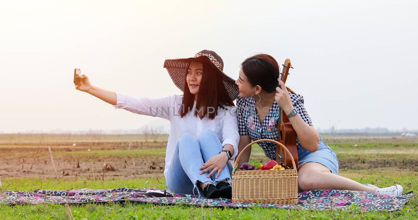 A group of Asian friends playing Ukelele and spending time making a picnic in the summer holidays.They are happy and selfie ,Relax time on holiday concept travel