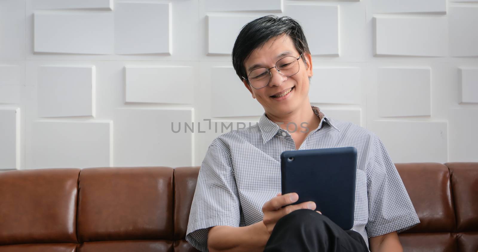 Senior Asian man playing tablet and video call on sofa in living room at home  Portrait of Asian elderly man is Relaxing and Happiness With playing tablet