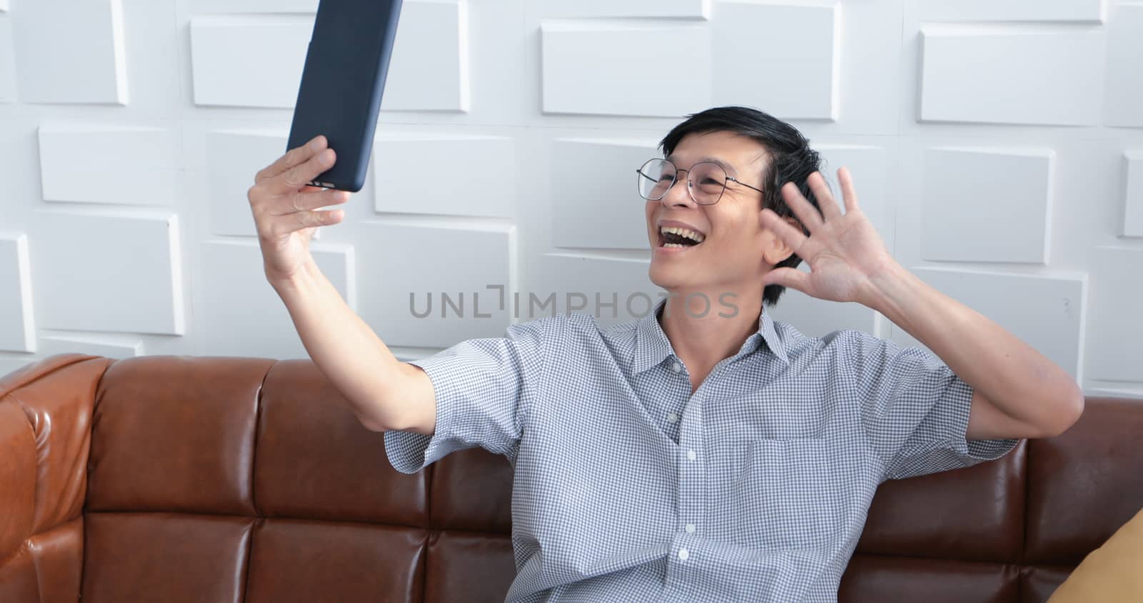 Senior Asian man playing tablet and video call on sofa in living room at home  Portrait of Asian elderly man is Relaxing and Happiness With playing tablet