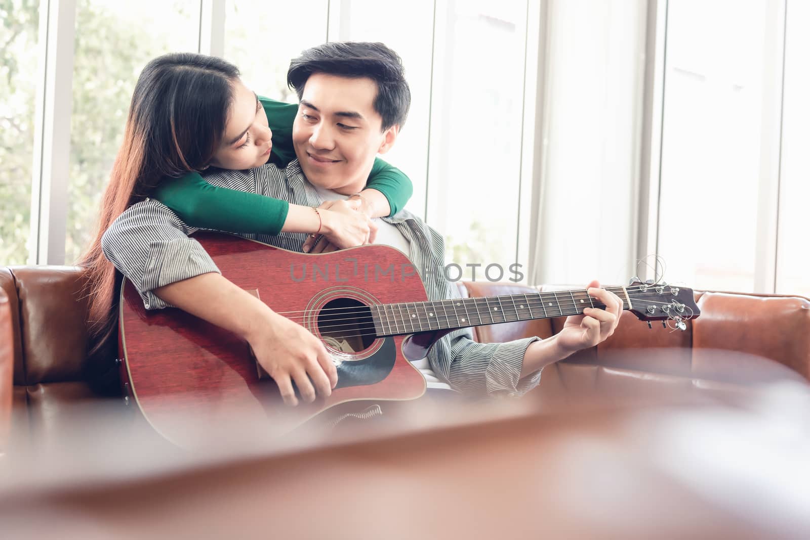 Young Couple Love Relaxing on Sofa in Living Room While Playing Guitar and Enjoyed Sing a Song at Home Together. Romantic Asian Couple Relaxation Enjoying Leisure Activity at Their Home. Stay at Home