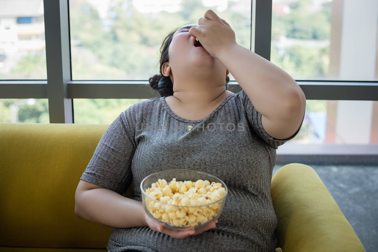 Overweight woman and asian girl enjoy eating food on sofa at home